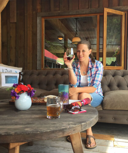 A woman holds a glass of wine while sitting on an outdoor patio.