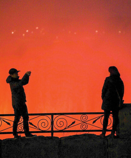 A man takes a photo of another person in front of an orange background.