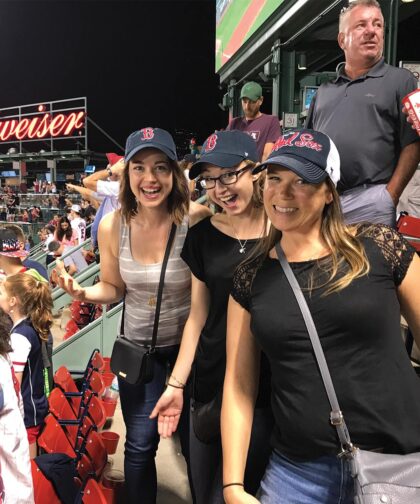Three people smile as they pose at a baseball game.