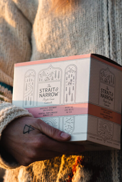Someone holds in their hand a box of Strait & Narrow drinks.